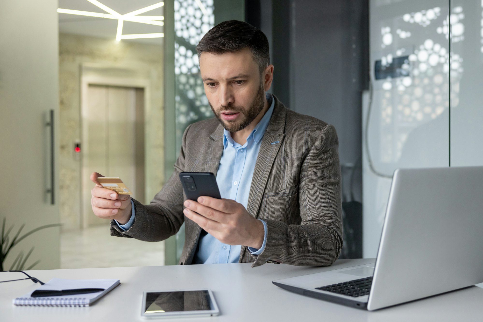 Businessman experiencing online fraud while checking smartphone and credit card