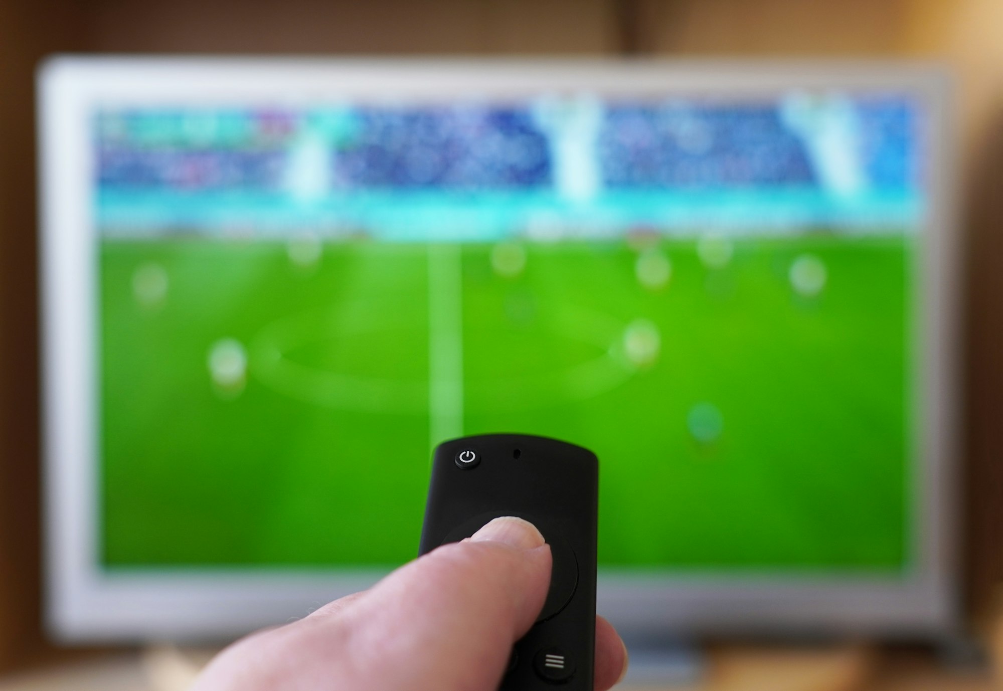 hand pointing remote control at tv with soccer match. football fan person watching game at home.