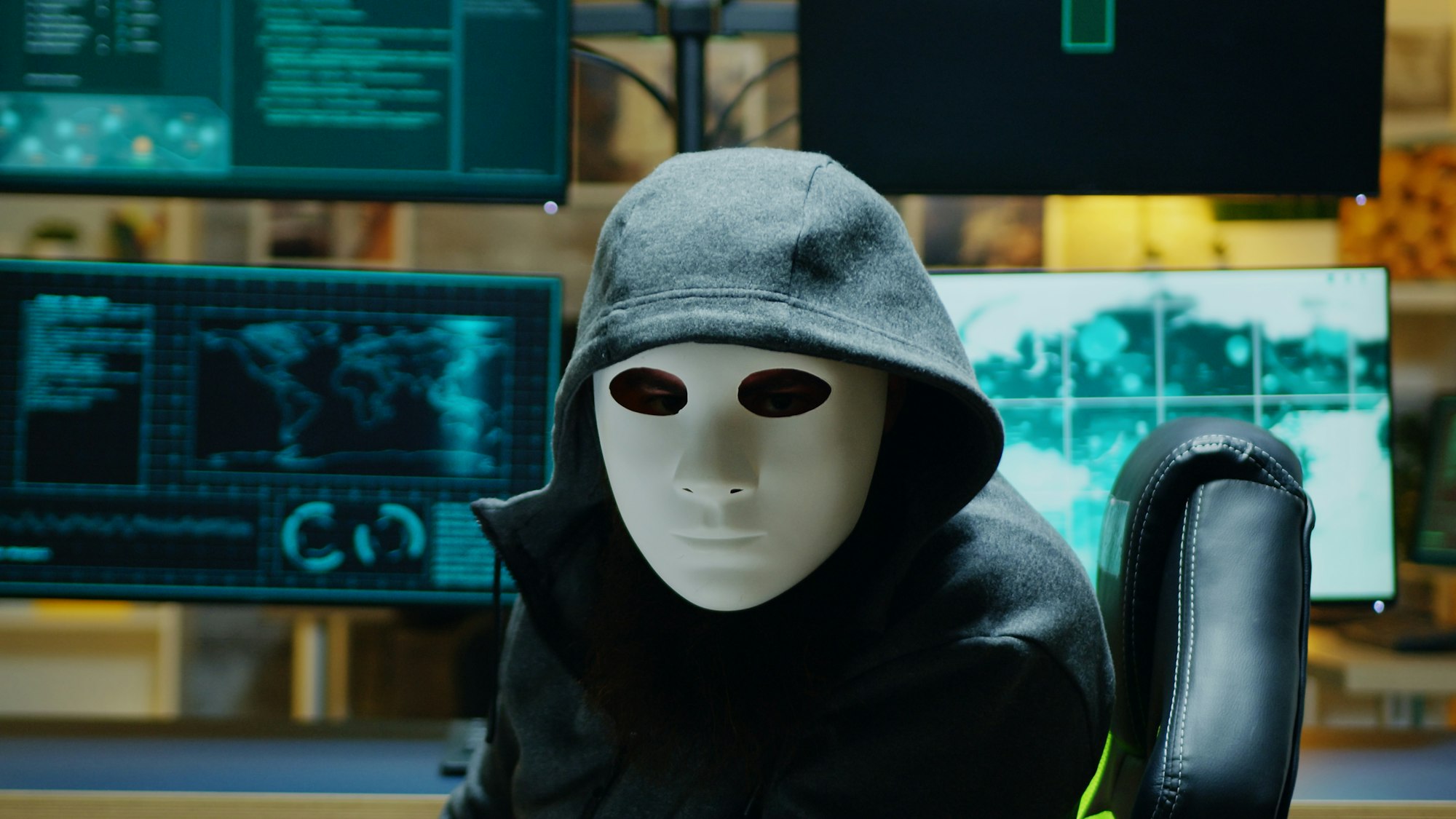 Masked hacker in his apartment looking into the camera